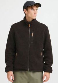 Veste en polaire noire avec un col haut, une fermeture �éclair à l'avant, des accents en bois et des poches latérales. Texture douce, coupe décontractée. Design casual.