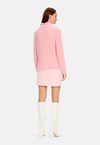 Rosa geripptes Rollkragensweatshirt, kombiniert mit einem hellrosa Rock und weißen knielangen Stiefeln. Der Pullover hat einen hohen Kragen und strukturierte Stoffoberfläche.