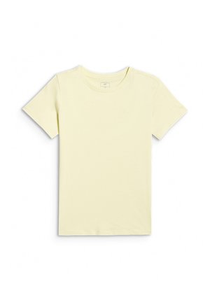 Jeune fille debout, vêtue d'un t-shirt jaune pâle, d'un pantalon évasé gris, de baskets blanches, tenant un sweat rose dans sa main gauche.