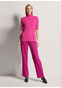 Fuchsiafarbenes, geripptes Rollkragenpullover mit kurzen Ärmeln und V-Muster; kombiniert mit passenden ausgestellten Hosen und schwarzen Stiefeln mit Absatz.