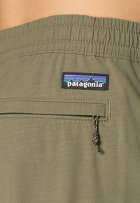 Olivgrön Patagonia-short med elastiskt midjeband, ficka med blixtlås och synlig varumärkeslogotyp nära midjan.