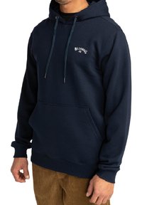 Sudadera de color azul marino con capucha con cordones, bolsillo frontal, puños acanalados y un pequeño logo blanco en el pecho. Hecha de material suave.