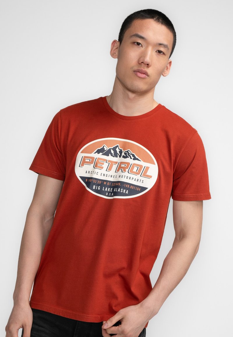 Camiseta de algodón roja con un estampado gráfico que presenta una silueta de montaña y el texto "PETROL". Manga corta, cuello redondo y corte relajado.