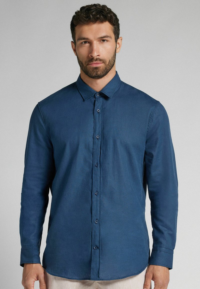 Långärmad, knappad skjorta i mörkblått tyg. Har en klassisk krage, framknappar och rak nederkant. Strukturerat, lätt material.