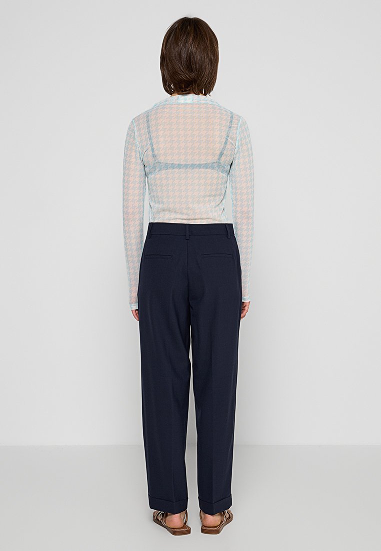 Langärmliges Mesh-Oberteil mit einem pastellfarbenen Hahnentrittmuster, kombiniert mit marineblauen Hosen; beide haben eine lockere Passform und minimale Details.