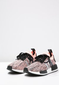 Pair of pink and black knit Adidas NMD sneakers with black laces and white cushioned soles, shown on white surface against plain background.
