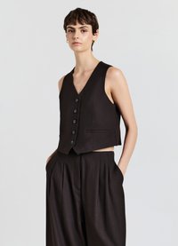 Schwarze ärmellose Weste mit V-Ausschnitt, ausgestattet mit sechs schwarzen Knöpfen und Seitentaschen, kombiniert mit hoch taillierten, weit geschnittenen Hosen.