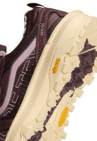 Gros plan d'une chaussure de randonnée marron et beige avec une tige Gore-Tex et une semelle Vibram présentant des profondes rainures pour l'adhérence.