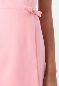 Robe rose en tissu lisse présentant un accent en nœud sur le côté avec un détail métallisé, mettant en valeur un design épuré et ajusté.
