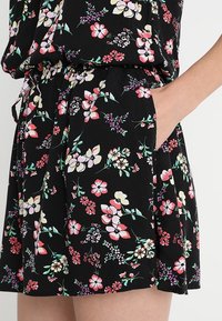 Svart blommig kjol med rosa, vita och lila blommor, med ett elastiskt midjeband och en hand som har placerats i sidofickan.