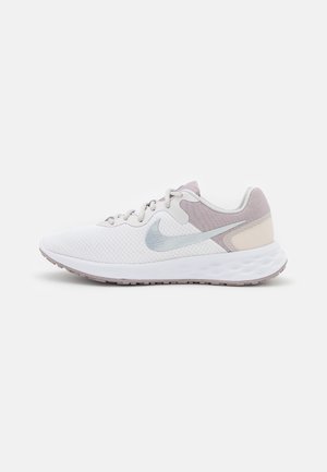 Zapatilla deportiva blanca con parte superior de malla, acentos de color morado claro, logotipo de swoosh plateado y una suela de goma texturizada diseñada para la comodidad.