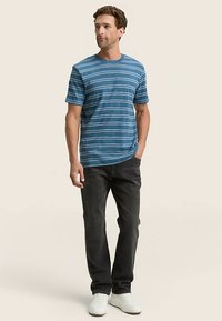 Modra črtasta bombažna majica z okroglim ovratnikom in kratkimi rokavi, v kombinaciji s temnimi kavbojkami in belimi športnimi copati.