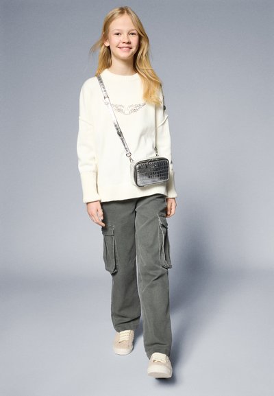 White knitted sweater with embroidered detail, gray cargo pants, and beige sneakers. Silver crossbody bag with crocodile texture.