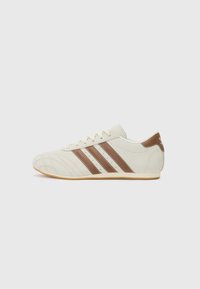 Hvide lædersneakers med brune ruskindstriber, tekstureret tå og lysebrun gummisål. Har snørrehuller og minimalistisk design.
