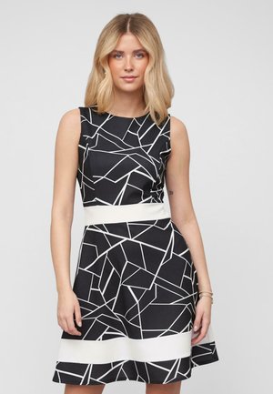 Robe noire avec des motifs géométriques abstraits blancs, design sans manches, corsage ajusté et ceinture blanche, jupe évasée. Tissu léger.