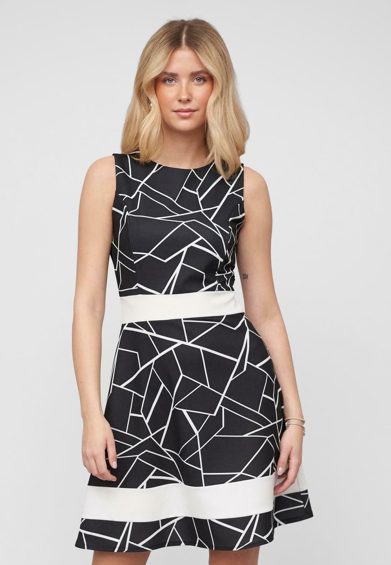 Robe noire avec des motifs géométriques abstraits blancs, design sans manches, corsage ajusté et ceinture blanche, jupe évasée. Tissu léger.