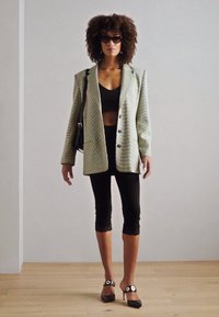 Grøn- og hvidstribet blazer med klapkrave, sort crop top, sorte blonde capri-bukser og sorte hælede sko med gulddetaljer.