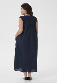 Navyblaues, ärmelloses Maxikleid mit gerafftem Rückendesign, fließendem Stoff und knöchellanger Schnitt. Sichtbare schwarze flache Schuhe.