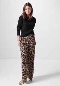 Schwarzer, gerippter Strickpullover mit rundem Halsausschnitt, kombiniert mit hoch taillierten, weit geschnittenen Leopardendruckhosen. Der beigefarbene Hintergrund setzt einen Kontrast.