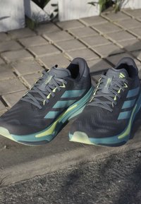 Black and teal athletic shoes with a textured upper, green accents, and a cushioned sole, featuring a lacing system and branding details.