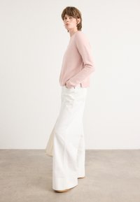 Pull en maille moelleuse rose clair avec un ourlet côtelé, associé à un pantalon large blanc à taille haute. Design simple sans motifs ni accessoires visibles.