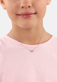 Sömmensilverhalsband med en rosa fjärilsberlock på en strukturerad kedja, bärs av ett barn med en ljusrosa skjorta.