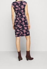 Marinblommig klänning med rosa accenter, korta ärmar, figursydd silhuett, knälång, ihop med bruna klackiga ankelstövlar.