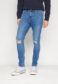 Vaqueros de denim azul desgastado con parches desgastados y un diseño ajustado. Combinados con zapatillas altas de color azul claro.