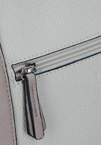 Bolso de cuero texturizado blanco con un bolsillo con cremallera. Presenta un tirador de cremallera plateado y acentos de cuero marrón a lo largo de los bordes.