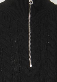 Czarny sweter z dzianiny z wysokim kołnierzem i srebrnym zamkiem błyskawicznym. Materiał ma teksturowany wzór w warkocz.