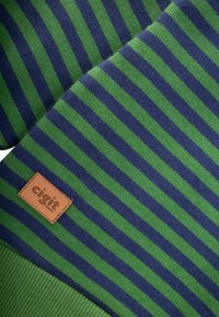 Zeleno-námornícky pruhovaný materiál s textúrovaným povrchom, s hnedou koženou nášivkou s nápisom "cigit."