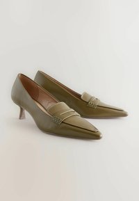 Olive rohelised nahast kontsad terava varbaga, millel on rihm üle toe ja väike läbipaistev stilettokonts.