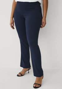 Navy tailored broek met een gladde textuur en een uitlopende pijpdesign, gecombineerd met zwarte strappy hakken. Eenvoudige, strakke lijnen zonder zichtbare patronen.
