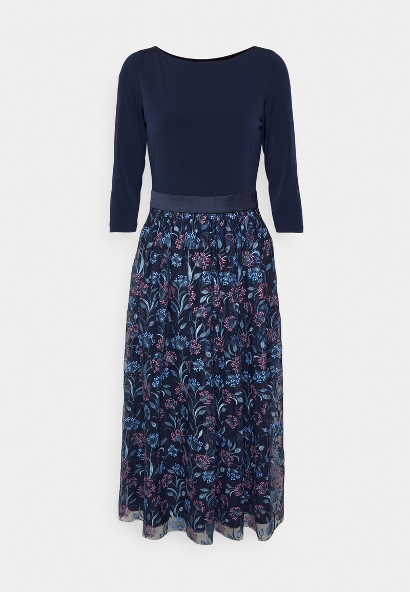 Robe bleu marine avec manches trois-quarts, corsage uni ajusté, ceinture en satin et jupe transparente à motif floral dans des tons bleus et violets.