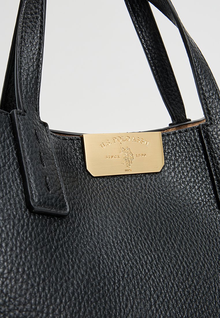 Bolso de mano de cuero negro con superficie texturizada, dobles asas y una placa de metal dorado con marca en relieve. Diseño compacto y estructurado.