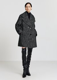 Cappotto doppiopetto in un motivo houndstooth bianco e nero, tessuto testurizzato, ampio colletto, tasche frontali, abbinato a stivali alti fino alla coscia neri e lucidi.