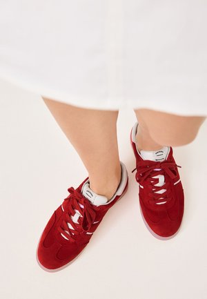 Scarpe sportive in suede rosso con accenti e lacci bianchi. Il design presenta una punta rotonda e una superficie texture.