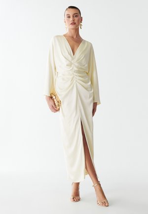 Knee-length, kreemikat dress, mille V-kaelus, pikad varrukad ja vöökohtadel kogutud detailid. Omab külgmisi lõhesid ja sujuvat, tekstuuriomast kangast.