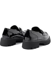 Scarpe di vernice nera con una grossa suola in gomma nera. Presentano una punta arrotondata e hardware decorativo sulla parte superiore, con una texture liscia.