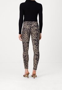 Leggings de estampado de leopardo con una textura suave y un diseño ajustado, combinados con una blusa negra de canalé y zapatillas de tacón marrones.