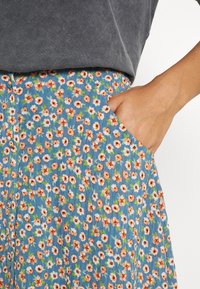 Blommig kjol med blå bakgrund och små orangea och vita blommor. Inkluderar en ficka och mjukt, texturerat tyg.