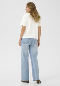Cremfarbendes kurzärmliges T-Shirt, kombiniert mit hellblauen, weit geschnittenen Jeans, von hinten betrachtet. Einfaches Design ohne sichtbare Muster.