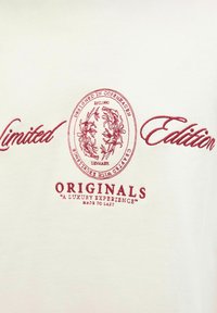 Tela color crema con bordado rojo. El diseño incluye "Edición Limitada", un emblema circular y "Originales" con un lema debajo.