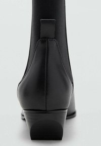 Stivale alla caviglia nero con tomaia in tessuto texturizzato e tacco in pelle. Presenta un piccolo anello sul retro e un tacco a blocco basso.