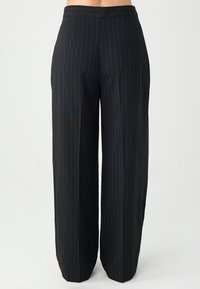 Czarne szerokie spodnie w paski o gładkiej fakturze, z płaskim pasem w talii i dwoma fałdami z przodu dla dodatkowego efektu.
