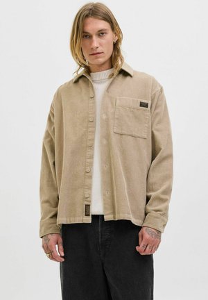 Beige corduroy shirt with a button-front design, collar, single chest pocket, and woven label. Long sleeves with buttoned cuffs.
