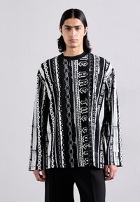 Dlhý rukáv košeľa s čiernobielou grafickou potlačou, ktorá obsahuje text, reťaze a pruhy, vyrobená z hladkej tkaniny. Okrúhly výstrih.