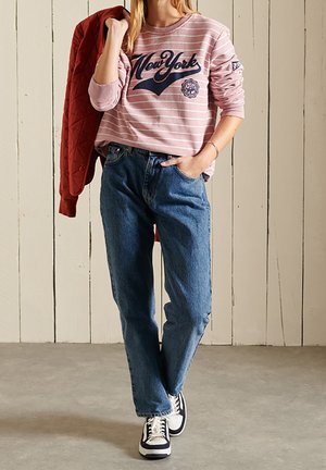 Rosa randig sweatshirt med "New York"-tryck, blå jeans i denim och svarta och vita sneakers. Jackan är röd med quiltad textur.