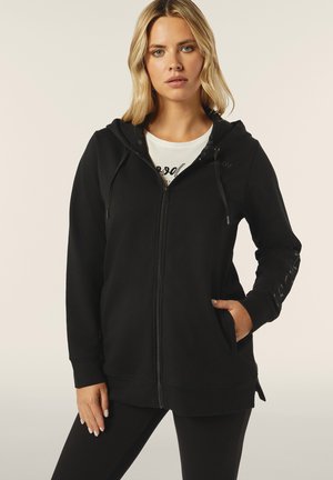 Haut à capuche zippé noir avec une poche avant, capuche à cordon et fentes sur les côtés. Caractérisé par un tissu doux et un logo en relief sur la poitrine.