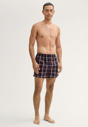 Geruite marineblauwe en rode boxershorts met een elastische tailleband, getoond op een staande figuur met blote huid.
